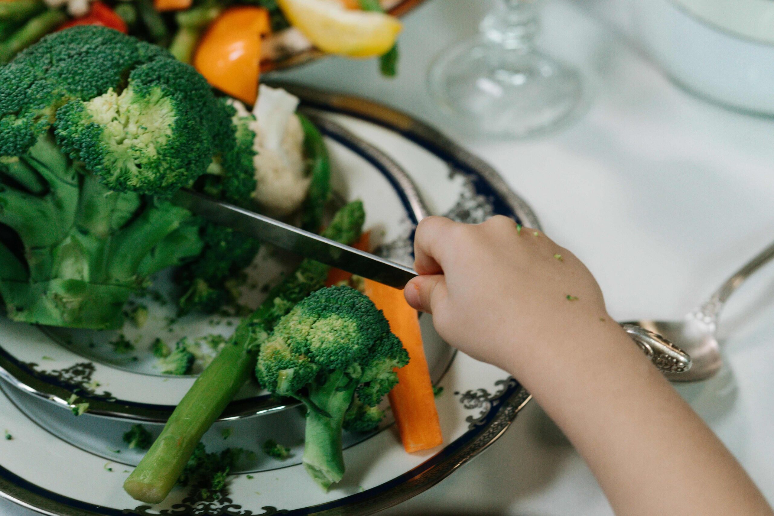 Plate of broccoli with children's hand holding cutlery